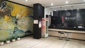 A reception area with a large abstract painting, a black reception desk, and a clock. There are potted plants and a vending machine. - Tai 9 Hotel (duelbert) (Dorbod County)