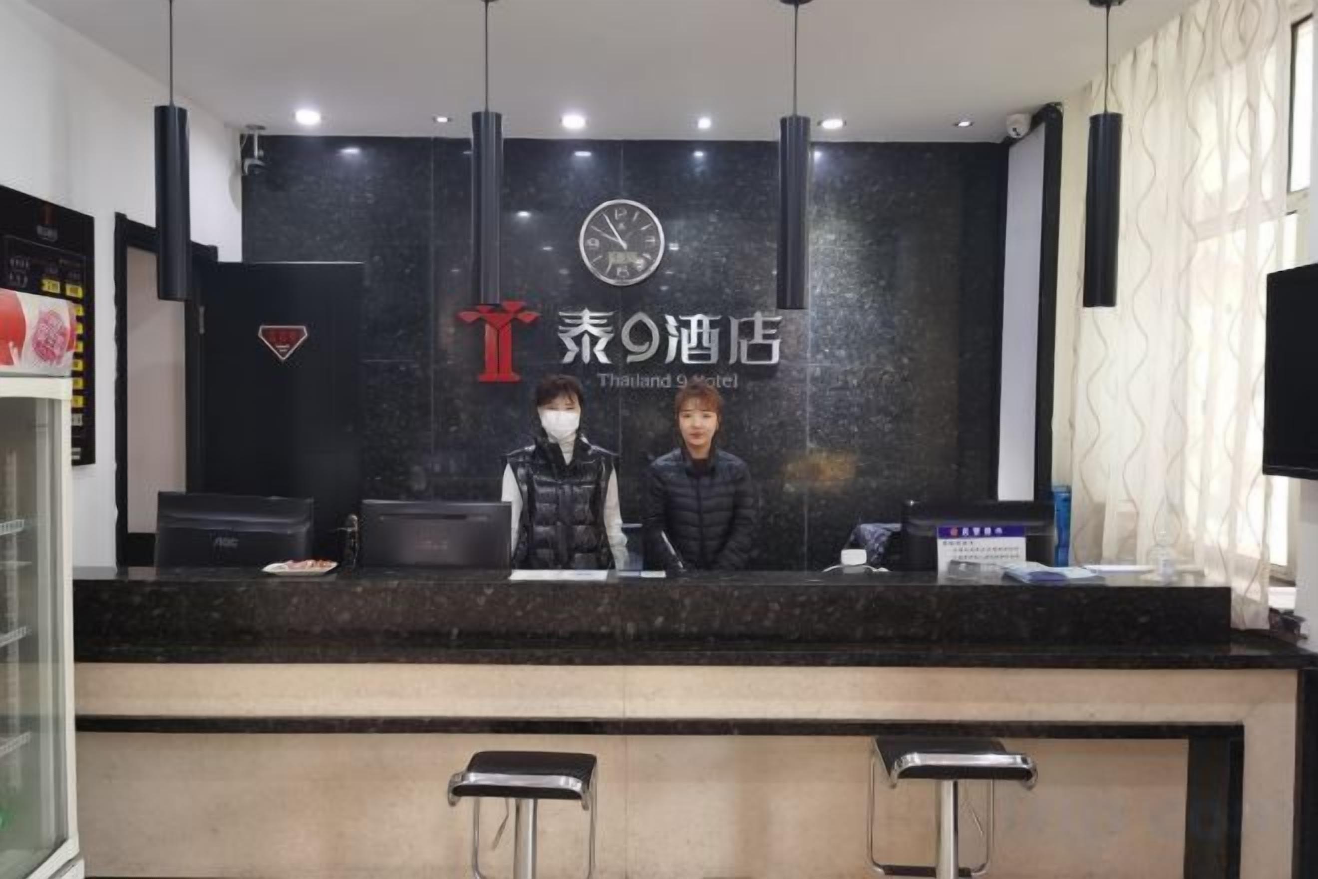 A hotel reception desk with a black counter, two bar stools, and a clock above the counter.