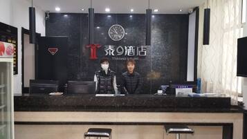 A hotel reception desk with a black counter, two bar stools, and a clock above the counter.