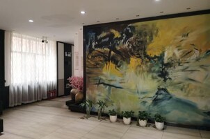 Um hall de hotel com uma grande pintura abstrata, plantas em vasos e piso de azulejos.