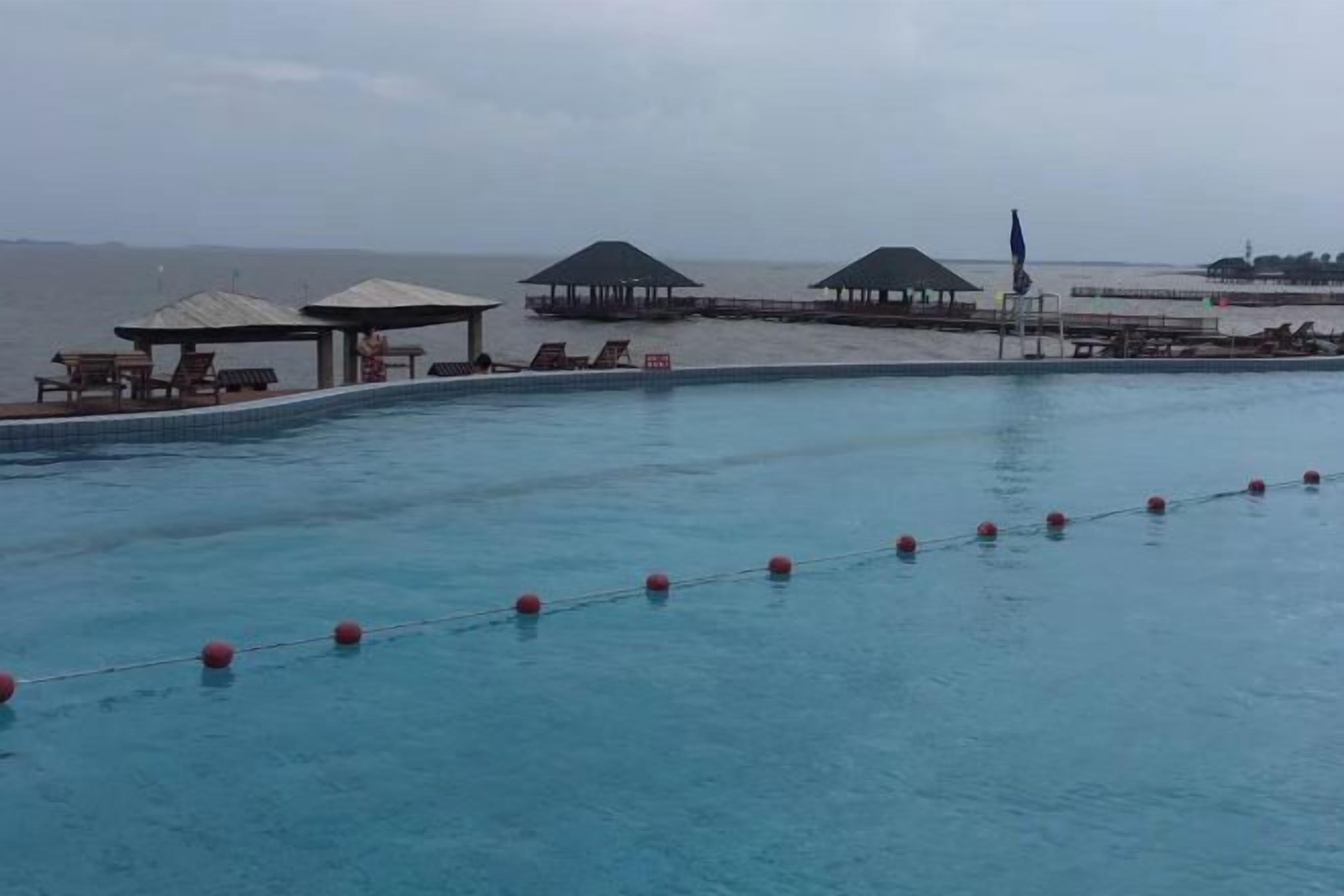 Piscina con vista al mar, sillas de descanso y zonas cubiertas.