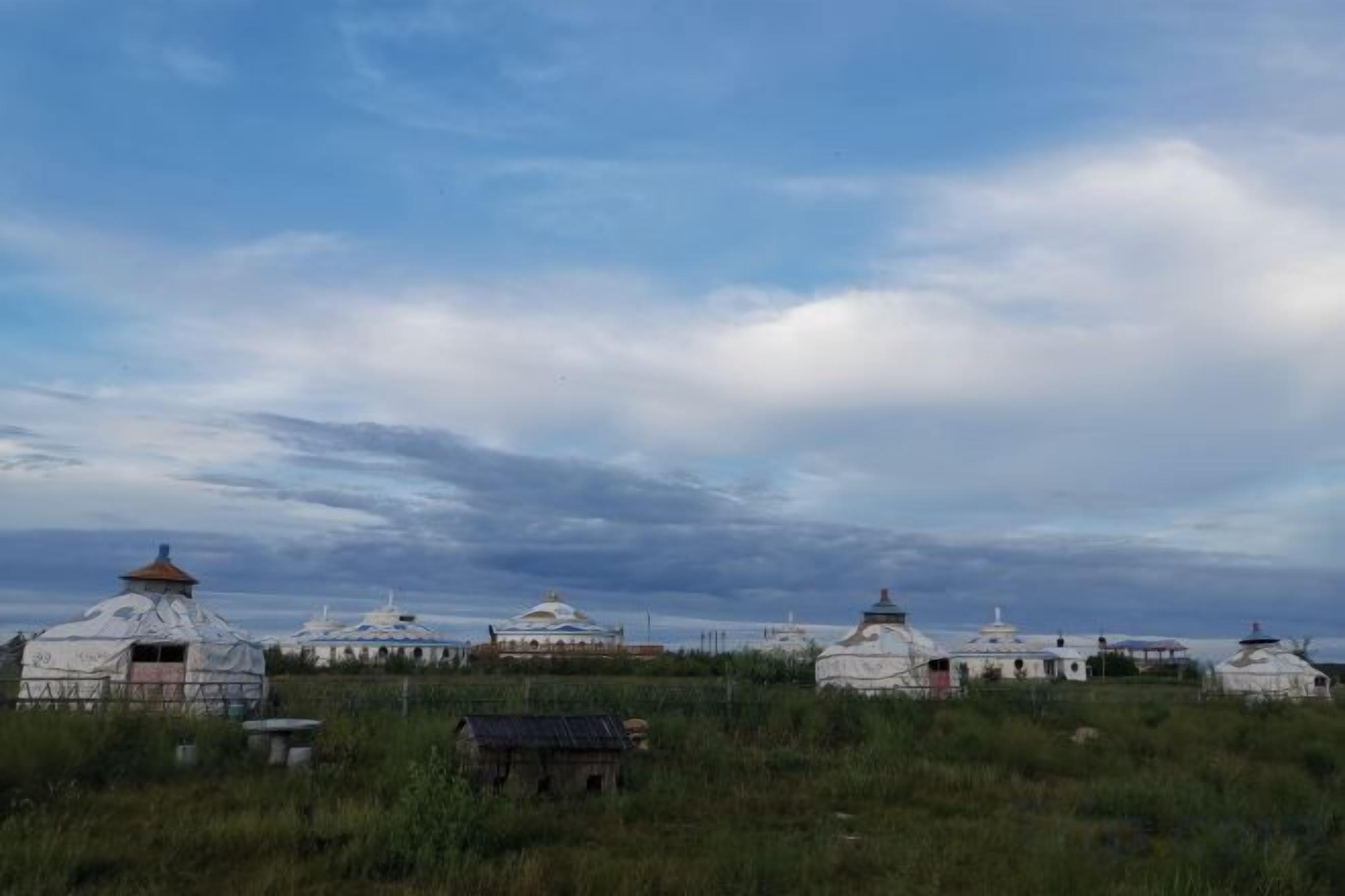 A series of traditional white yurts in a grassy field with a cloudy sky.