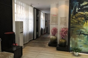 A hallway with a reception desk, a large painting, and a potted plant. - Tai 9 Hotel (duelbert) (Dorbod County)