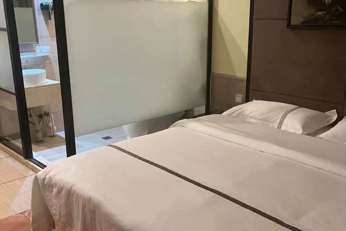 A hotel room with a bed, a bathroom visible through a glass partition, and a wall-mounted picture.