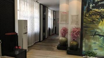 A hallway with a reception desk, a large painting, and a potted plant.