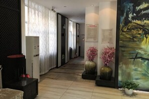 A hallway with a reception desk, a large painting, and a potted plant. - Tai 9 Hotel (duelbert) (Dorbod County)