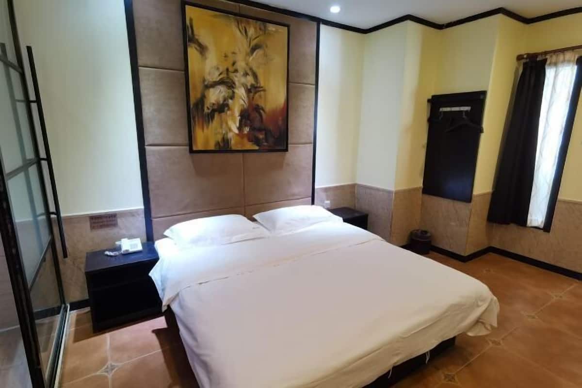 A hotel room with a bed, a nightstand, a wall-mounted painting, a wardrobe, and a window with curtains.