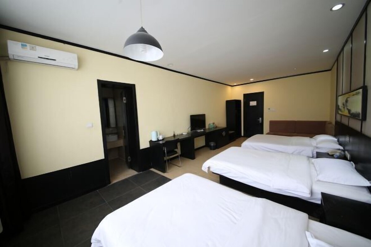 A hotel room with two beds, a desk, a chair, a TV, and an air conditioning unit.