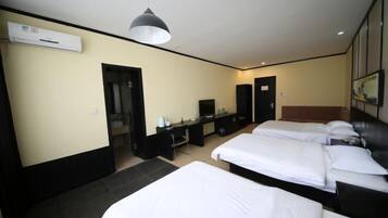 A hotel room with two beds, a desk, a chair, a TV, and an air conditioning unit.
