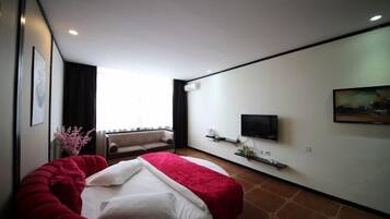 A modern hotel room with a large bed, a sofa, a TV mounted on the wall, and a window providing natural light.