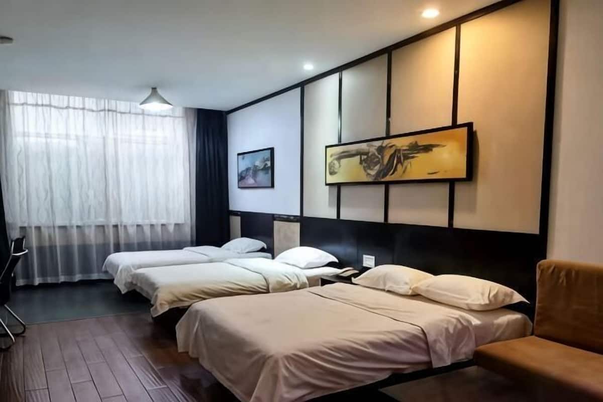 A hotel room with two beds, a sofa, a desk, and a window with sheer curtains.