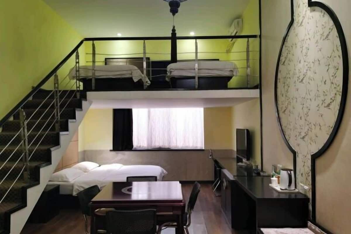 A compact hotel room with a bunk bed, a desk, a chair, a television, and a large mirror.