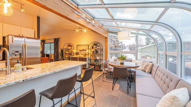 A modern kitchen with a glass ceiling, a central island, bar stools, and a seating area with a sofa and table.