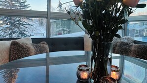 A glass table with a vase of roses and candles, a chair, and a view of a snowy landscape through large windows.