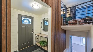 A modern interior with a wooden staircase, a console table with plants, and a view to the outside.
