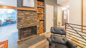 A modern living room with a stone fireplace, a black leather chair, and a dining area with a wooden table and chairs.