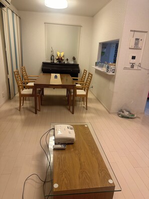 Ein Essbereich mit einem Klavier, einem Projektor und einem kleinen Tisch mit Stühlen.