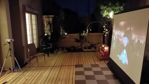 Un área de patio exterior con terraza de madera, una pantalla de proyector y un espacio de estar con sillas.