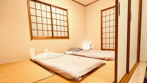 Una habitación japonesa tradicional con suelo de tatami, dos camas, puertas correderas y una mesita de noche con lámpara.