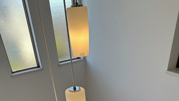 Una habitación con techos altos, tres lámparas colgantes, un banco de madera con revistas y vistas a un pasillo con una puerta y una ventana.