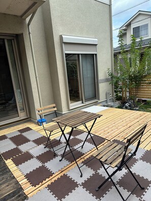 Eine Terrasse mit einem Holztisch und Bänken, einer Schiebetür aus Glas sowie einem Fenster mit Jalousien.