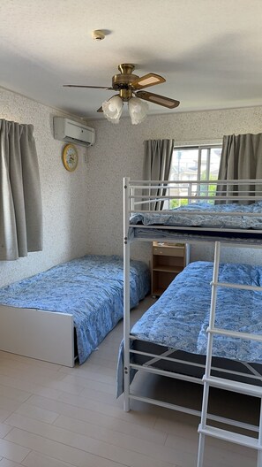 Ein Zimmer mit Etagenbetten, Deckenventilator, Klimaanlage, einer Uhr und einem Fenster mit Vorhängen.