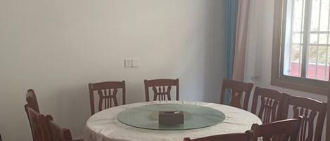 Una mesa de comedor redonda con cubierta de vidrio, rodeada de sillas de madera.