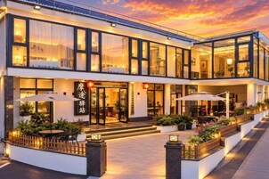 A hotel with a modern design, featuring a two-story structure, outdoor seating area, and a well-lit entrance.