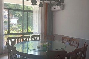 Una mesa de vidrio redonda con seis sillas, una ventana con cortinas y un aire acondicionado instalado en la pared.