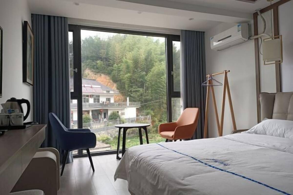 Een hotelkamer met een bed, een bureau, een stoel, een klein tafeltje en uitzicht op een bebost gebied.