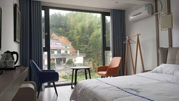 Habitación de hotel con cama, escritorio, silla, una mesita y vistas a un área boscosa.