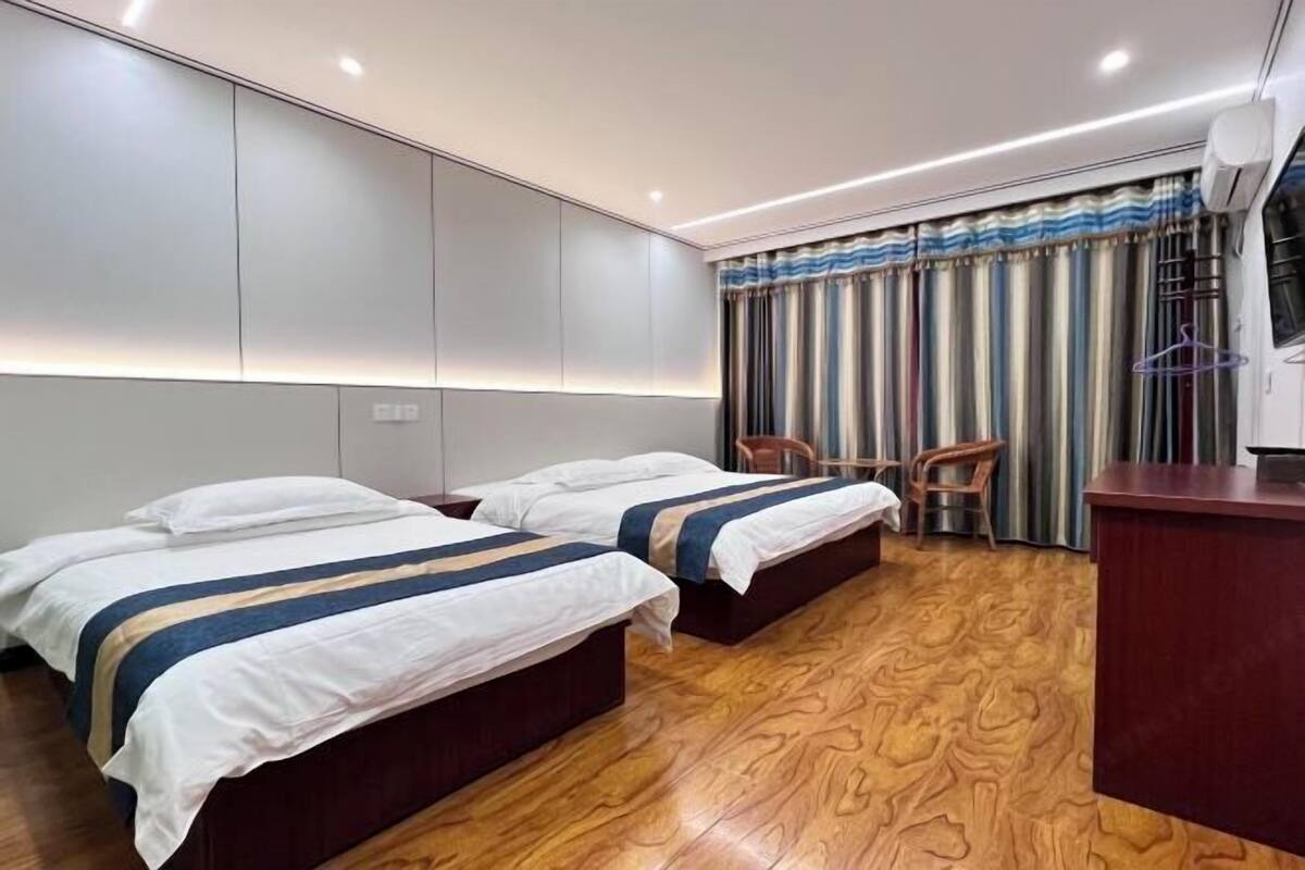 Een hotelkamer met twee bedden, een houten vloer, een bureau en een gordijn met strepen.