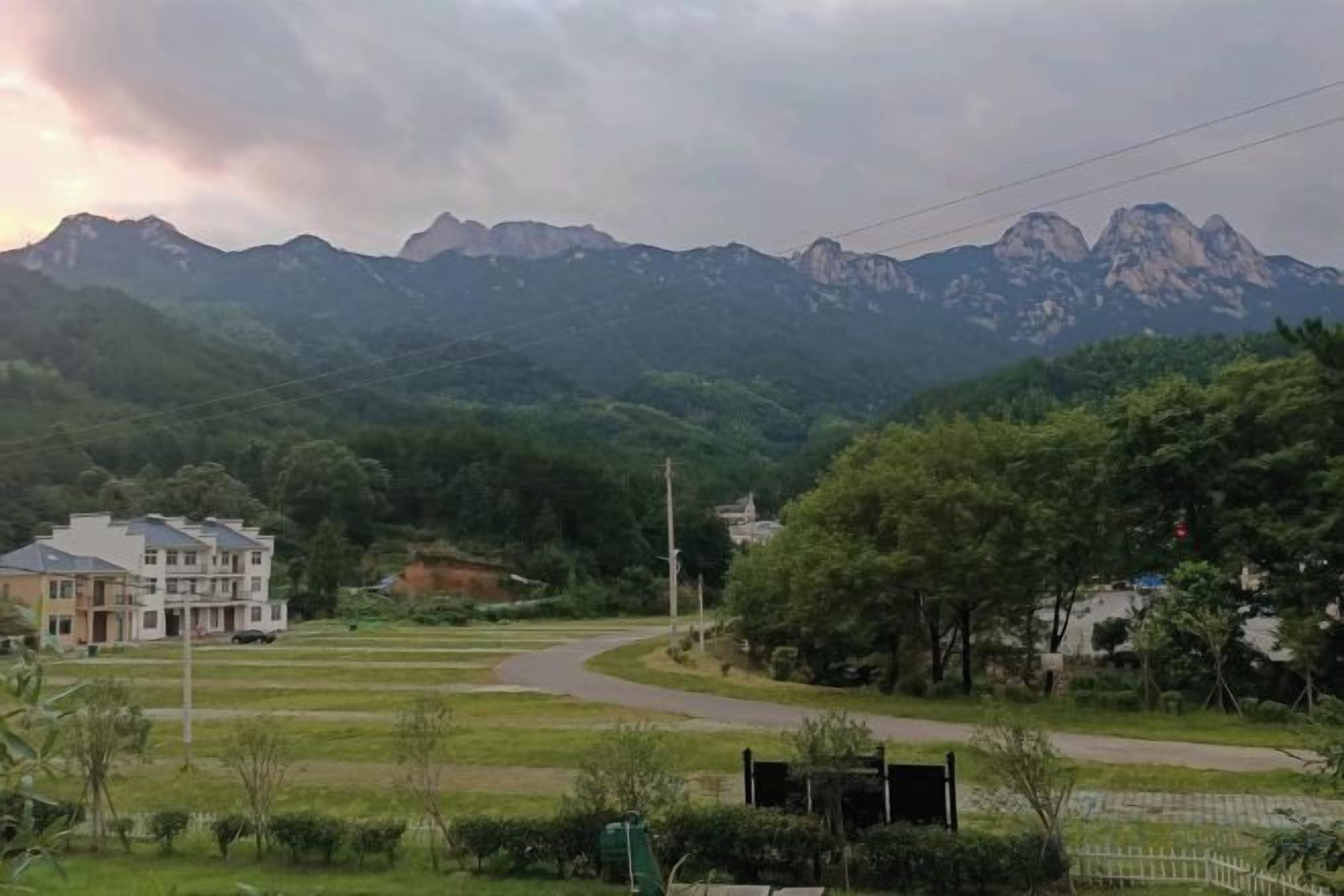 A residential area with a curved road, houses, and a mountain range in the background.