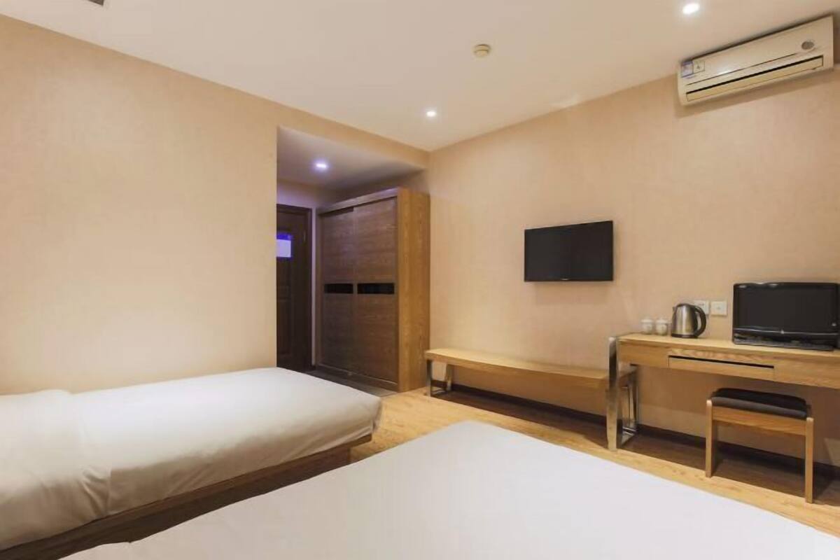 Ein Hotelzimmer mit zwei Betten, einem Schreibtisch mit Stuhl, einem Fernseher und einer Klimaanlage.