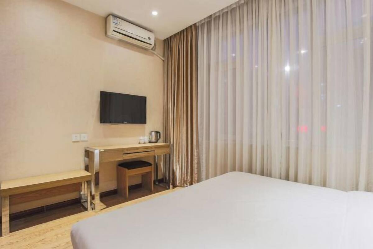 Ein Hotelzimmer mit Bett, Schreibtisch, Stuhl, Fernseher und einem Fenster mit Vorhängen.