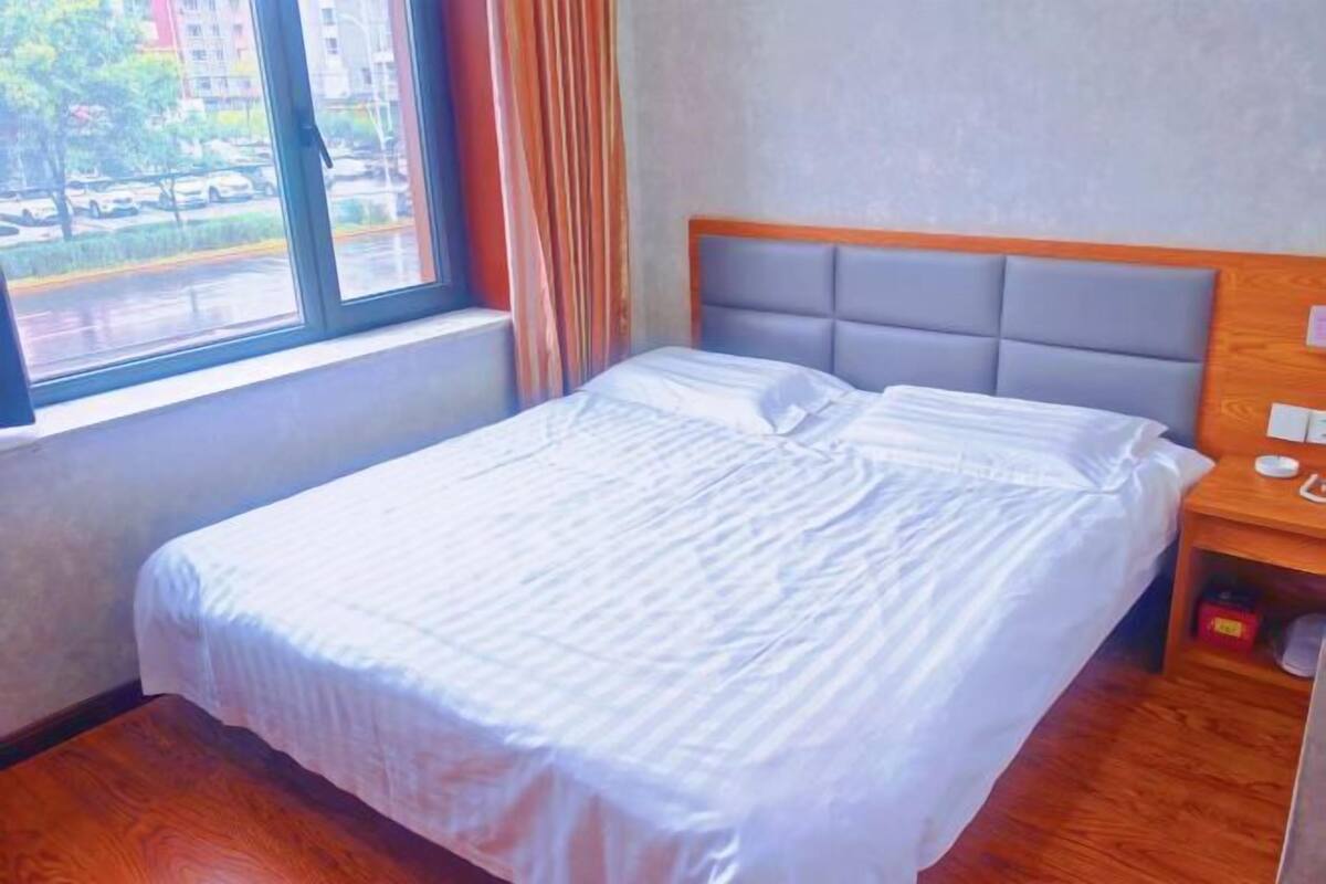 Ein Hotelzimmer mit Bett, Nachttisch, Fenster mit Vorhängen und Blick auf die Straße.