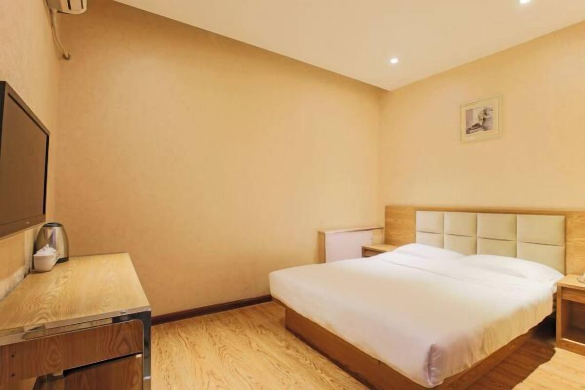 Ein Hotelzimmer mit einem hölzernen Bett, einem Nachttisch, einem kleinen Schreibtisch und einem an der Wand befestigten Fernseher.