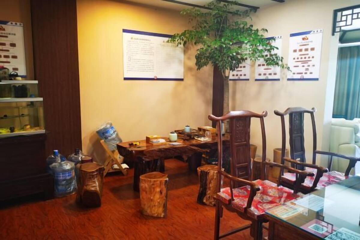 A room with a wooden dining table, chairs, a potted plant, and a bulletin board with notices.