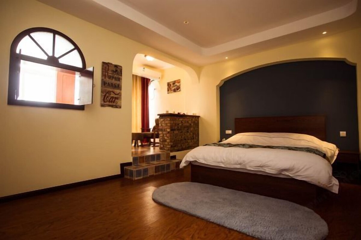 Ein Schlafzimmer mit einem Bett, einem Fenster, einem Steinofen und einer Treppe zu einer oberen Ebene.