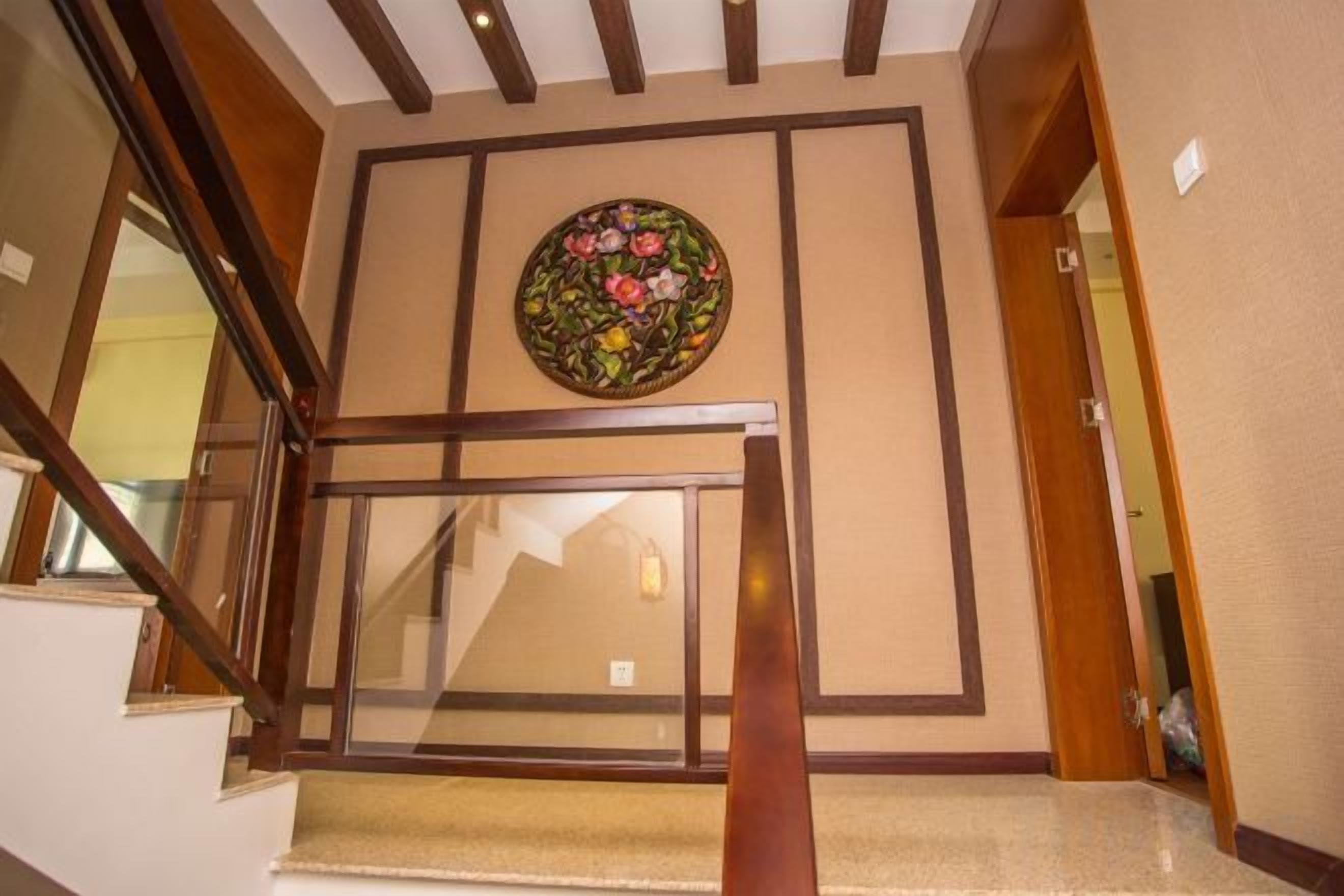 A staircase with a wooden handrail and a glass balustrade, leading to a room with a beige wall and a circular floral artwork.