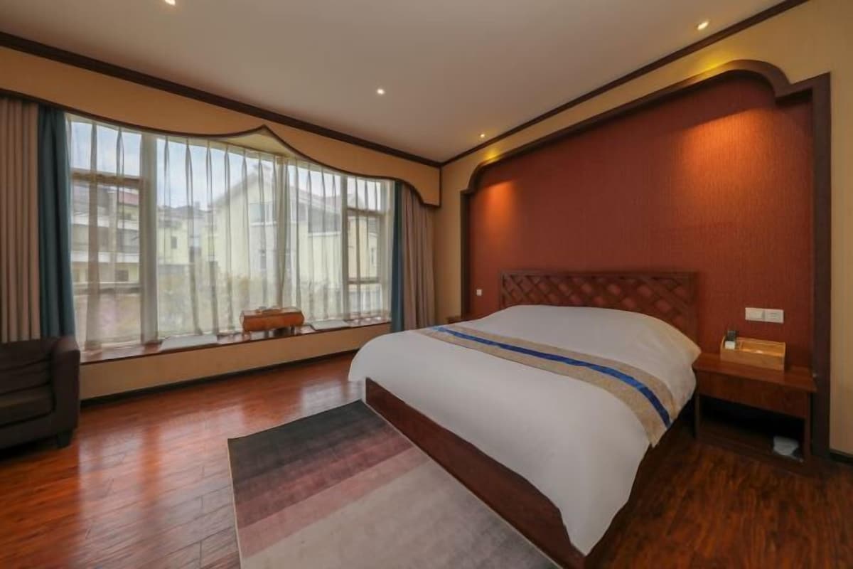 A hotel room with a large bed, a window with curtains, a wooden floor, and a nightstand.
