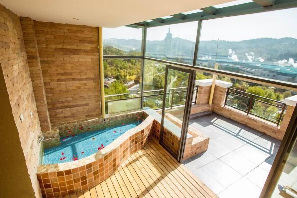 A balcony with a hot tub, glass walls, and a view of a cityscape.