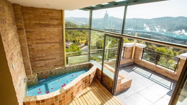 A balcony with a hot tub, glass walls, and a view of a cityscape. - Qianshan Yihao Villa (Yuxi)