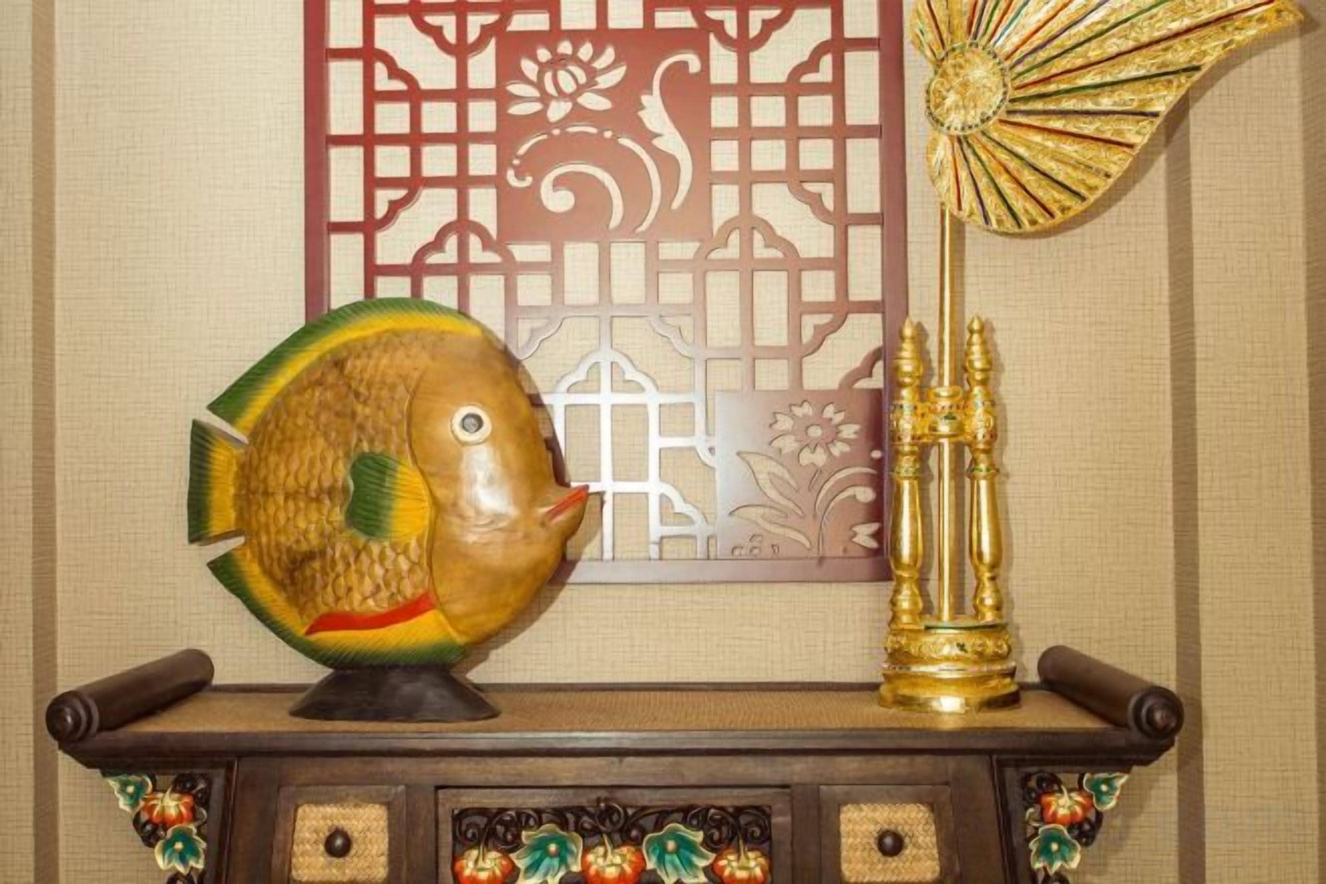 A decorative fish on a shelf, a golden fan, and a traditional wall panel.