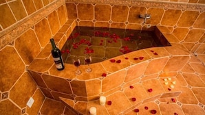 A stone-floored jacuzzi with rose petals scattered on the floor and a bottle of wine and glass on the edge. - Qianshan Yihao Villa (Yuxi)