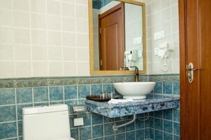 Un baño con inodoro blanco, un lavabo con encimera de mármol, un espejo y un perchero para toallas.