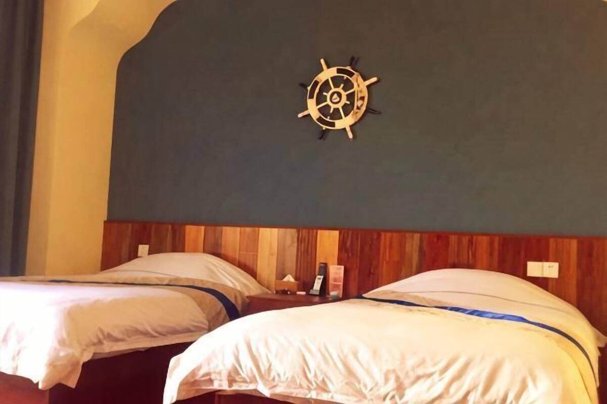 Two single beds with wooden headboards, a wall-mounted ship's wheel decoration, and a small bedside table with a lamp.