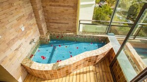 A hot tub with a stone mosaic border, wooden deck, and a glass railing overlooking a residential area. - Qianshan Yihao Villa (Yuxi)