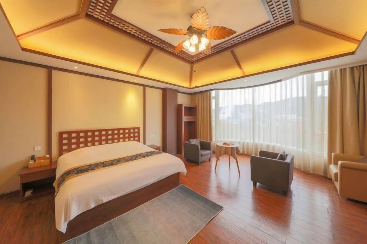 A hotel room with a large bed, a ceiling fan, a small table, and a sofa.