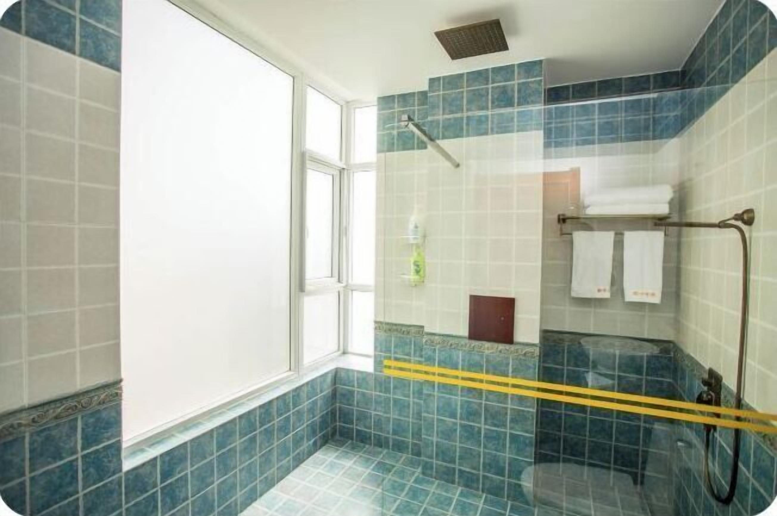 A bathroom with blue tiles, a glass shower enclosure, a window, and a towel rack with towels.